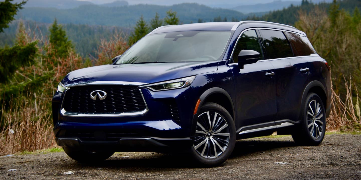 2023 Infiniti QX60 Sensory AWD in dark blue. The SUV is against a forested, mountainous background